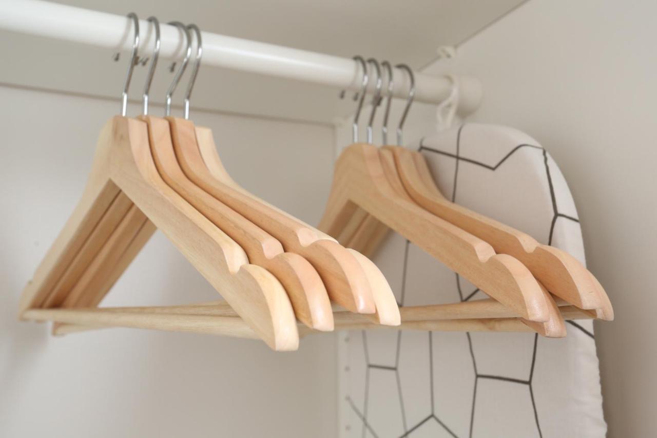 Wooden hangers on a wardrobe rail with a folded ironing board behind