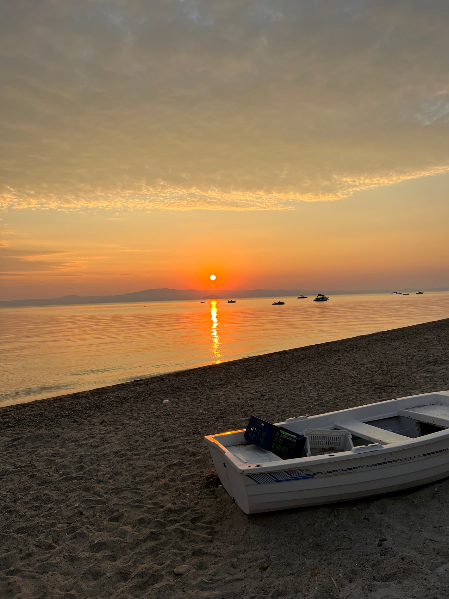 Sunrise over the calm sea at Polychrono beach, a small white boat resting on the sand