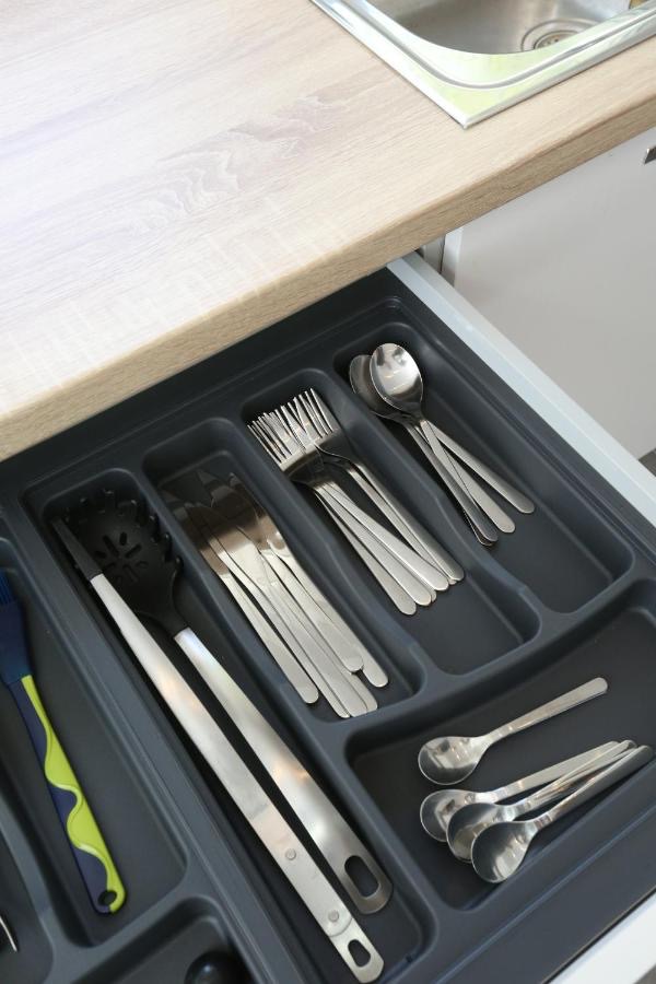 Open kitchen drawer with a cutlery tray holding forks, knives, spoons and serving utensils beside the sink
