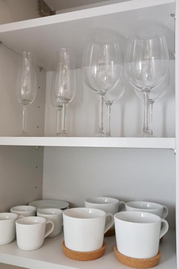 Kitchen cabinet shelves stacked with wine glasses, champagne flutes and white mugs on cork coasters